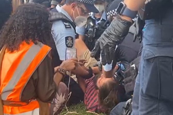 Police officers pin a bearded man onto the ground.