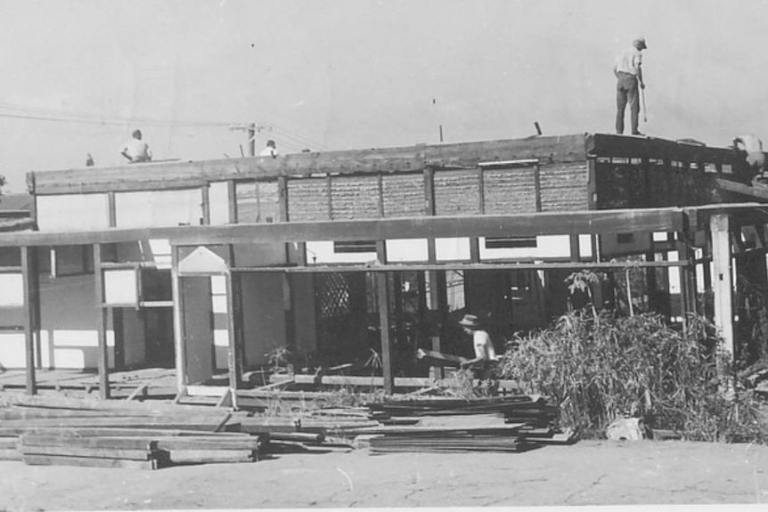 A black and white photo of workers dismantling a single-storey house