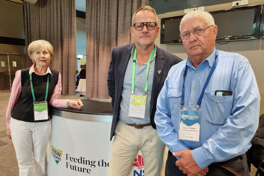 A woman and two men standing at a conference, wearing lanyards around their necks.