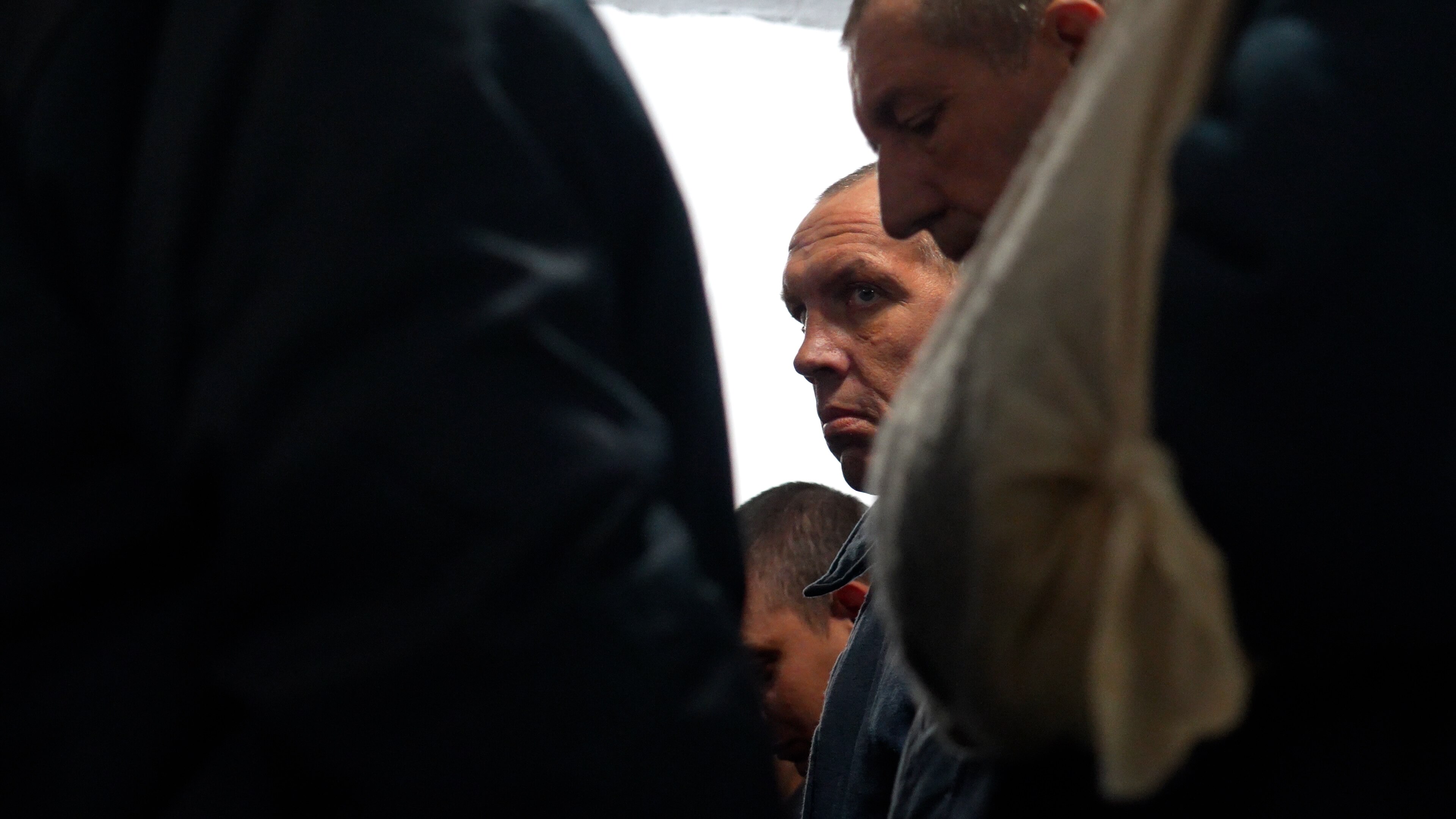 A grim-faced man stands in line in a Ukrainian facility for prisoners of war.