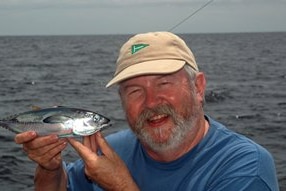 Man holding a fish out on the water, he's smiling.
