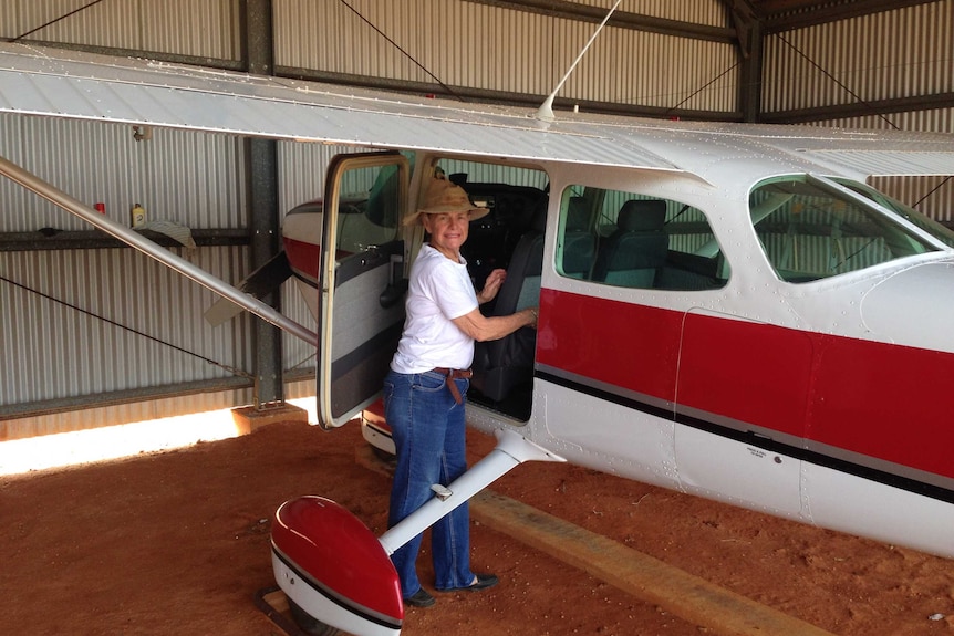 Penny Button stands at the door of a red and white light plane.