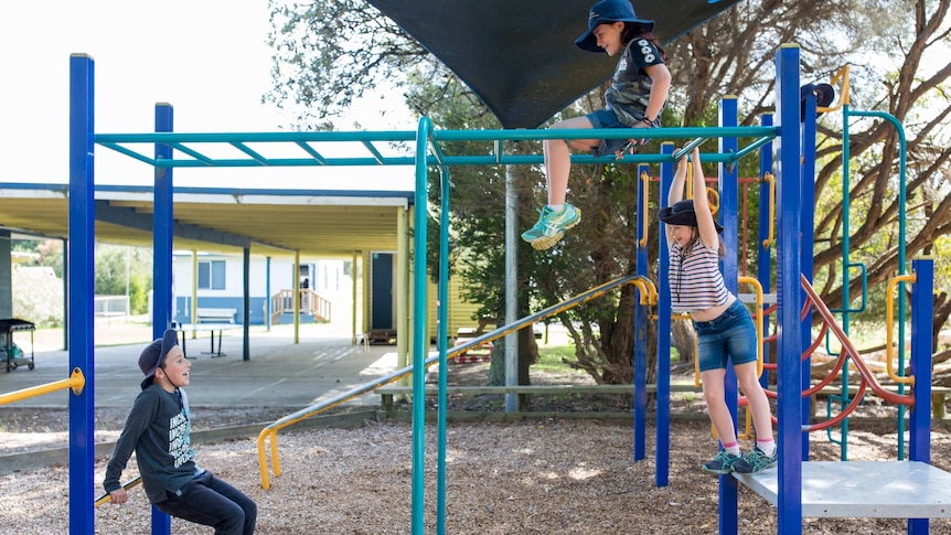 A student sits atop the monkey bars, another hangs from the bars and a third leans on a platform, talking.