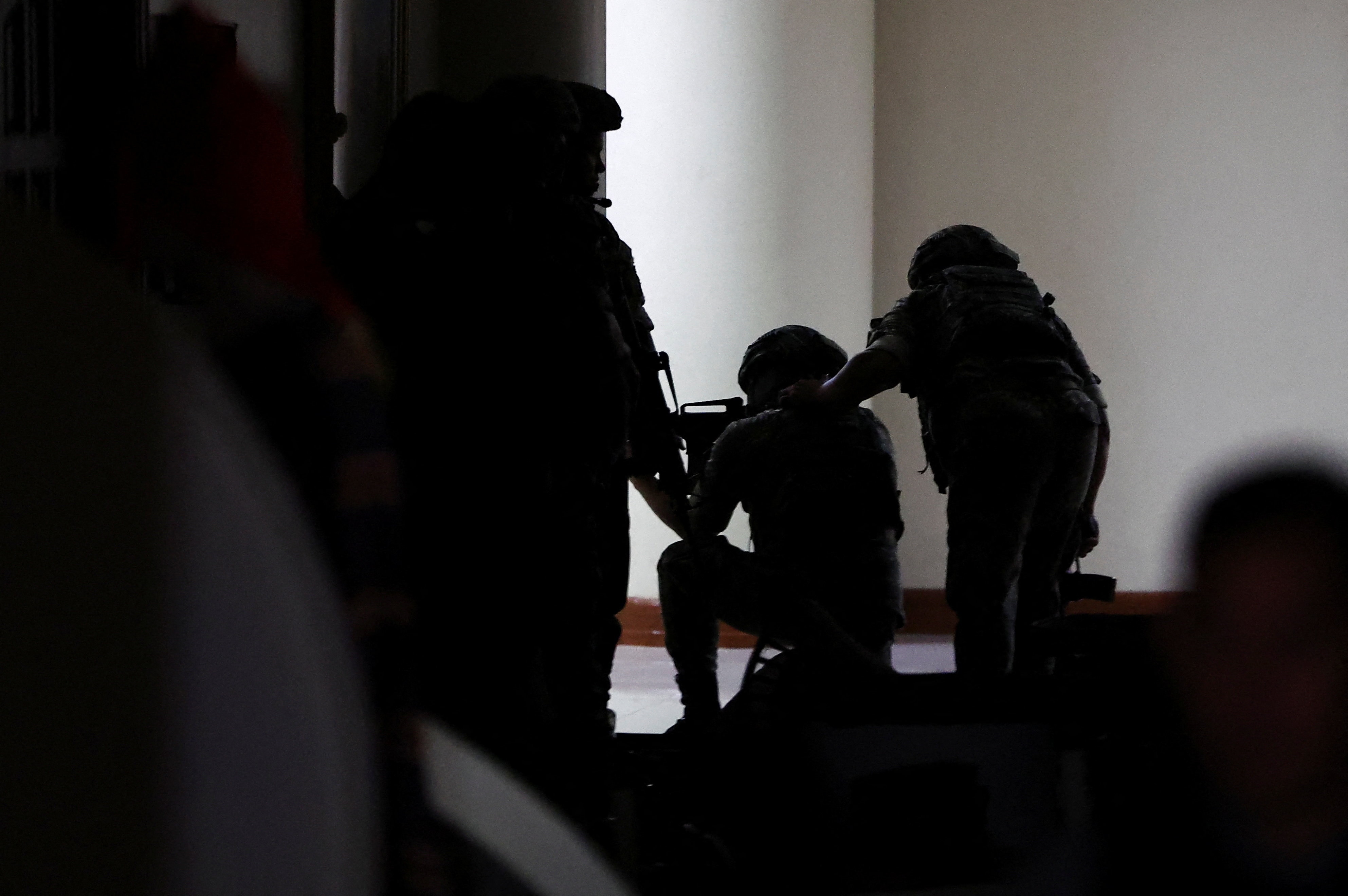 Silhouettes of people in uniform holding guns inside a building.