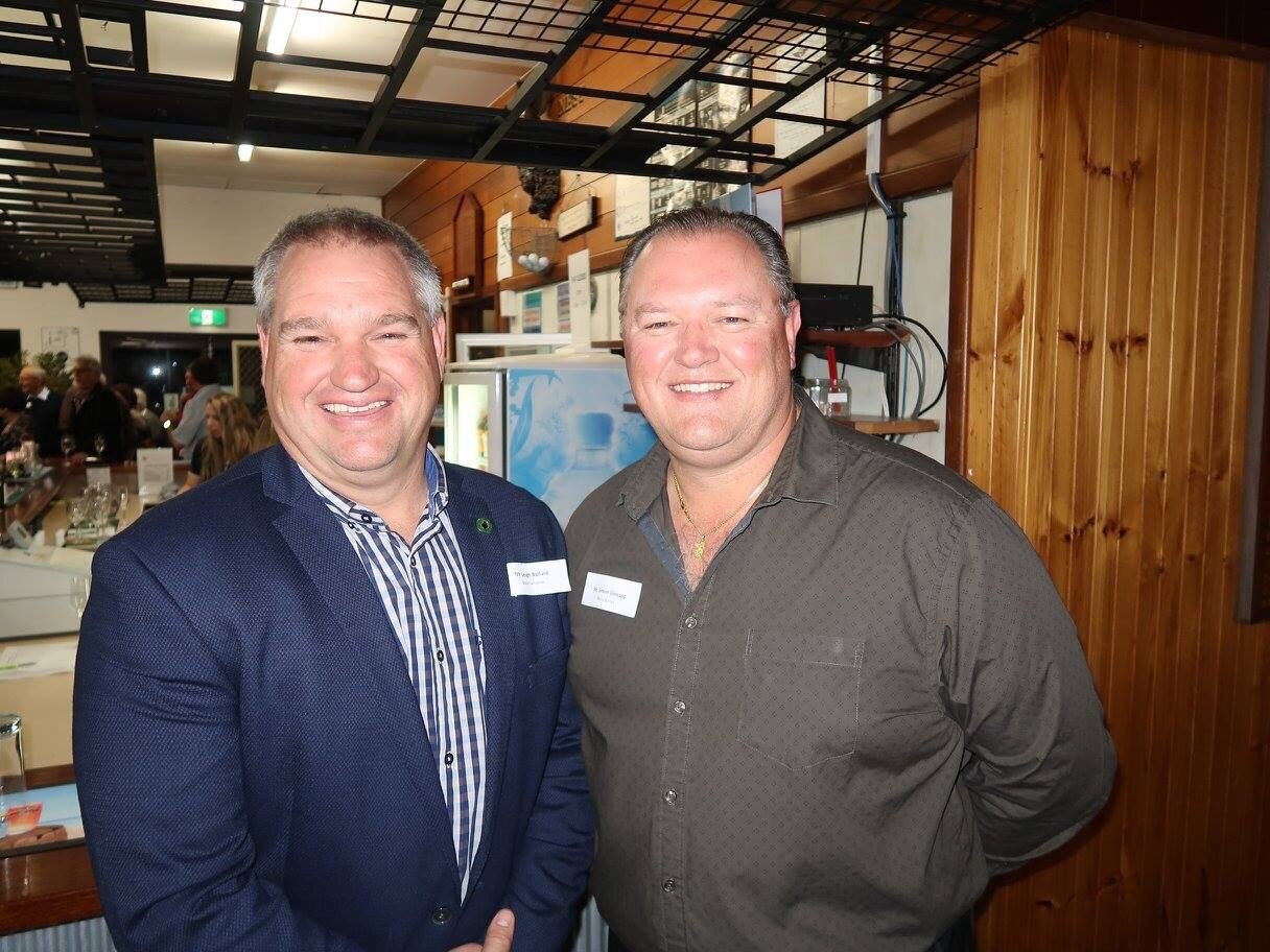 Dos hombres sonríen mientras posan en un salón rural.