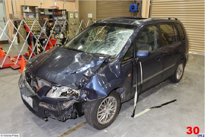 A small dark blue car which has been badly damaged in a crash and has a cracked windscreen.
