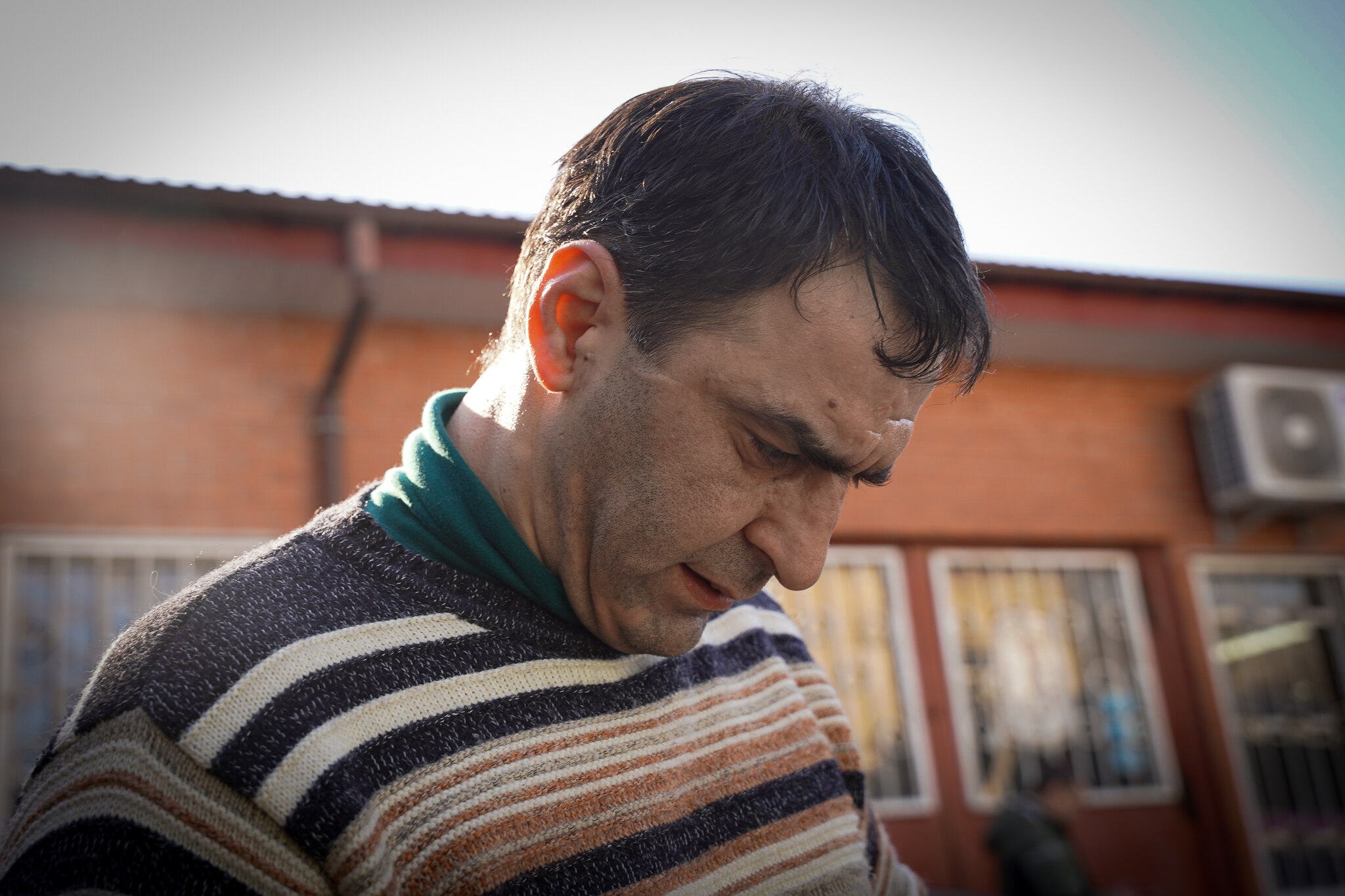 A man looks down at his phone with the sun behind him. 