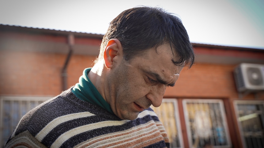 A man looks down at his phone with the sun behind him. 