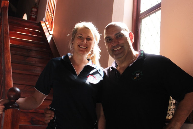 A man and a woman standing on wooden stairs with a sunlit window in the background.