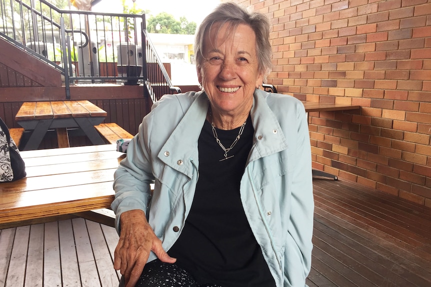 72-year-old Brisbane woman Diane Burmeister smiles as she sits on a bench.