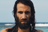 Colour still of Behrouz Boochani holding a fish by the ocean from video artwork Remain by artist Hoda Afshar.