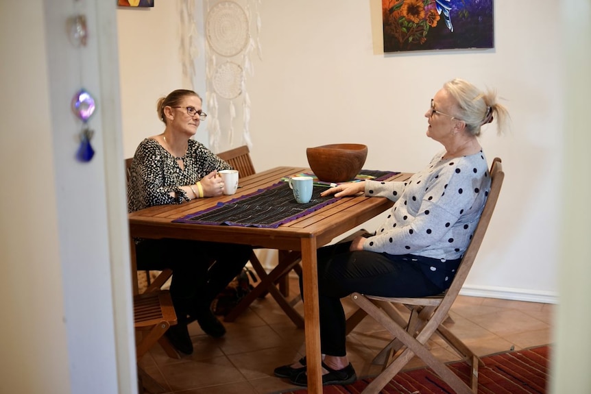 Two women sitting at a table holding white mugs