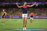 A Melbourne AFL player stands on tiptoe and roars in celebration pointing his fingers in the air.