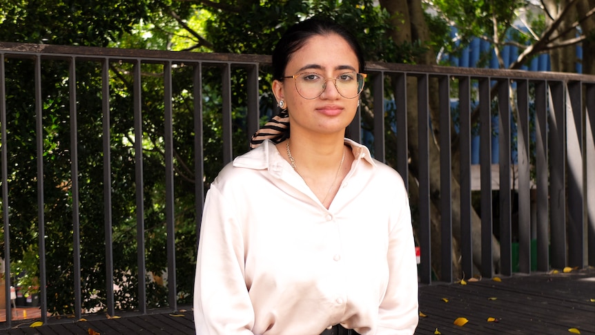 Young woman, Lina, wearing glasses, with railing and trees in background.