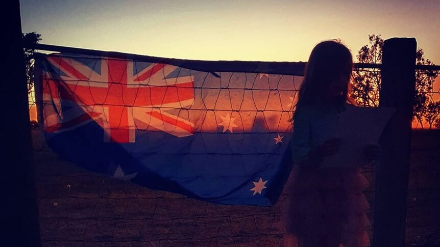 A little girl watches the sunrise over an Australian flag on a cattle property near Charters Towers.