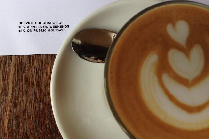 Image shows a cup of coffee and a menu noting surcharges of 10 percent for weekends and 18 per cent for public holidays apply.