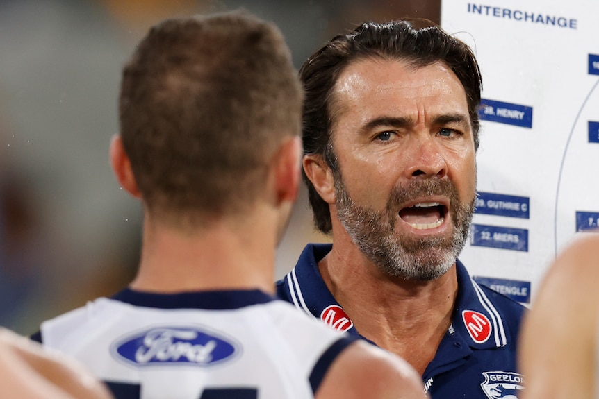 Chris Scott shouts at one of his players with a tactics board behind him