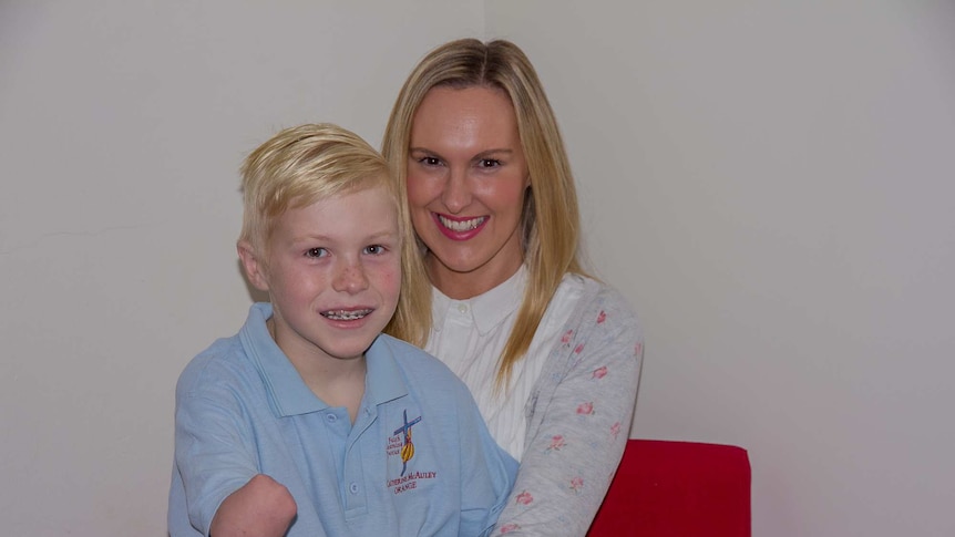 A boy with an amputated forearm sits on his mother's lap