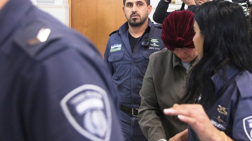 Malka Leifer bows her head down as she is escorted by police through a door.