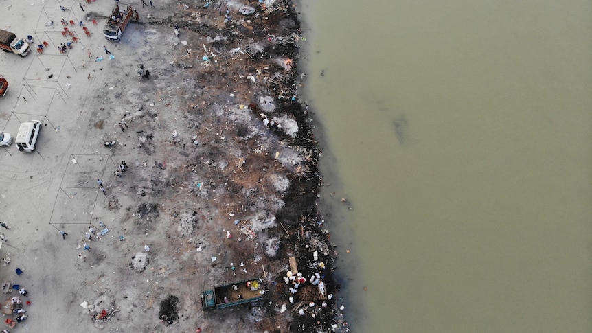 The banks of a river are grey with ash and littered with debris.