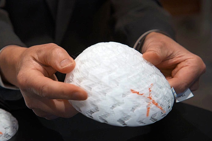 An intricate, plastic-looking scaffold in the shape of a breast is held by a scientist.