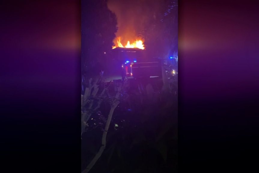 Flames leap into the night sky from the roof of a burning house.