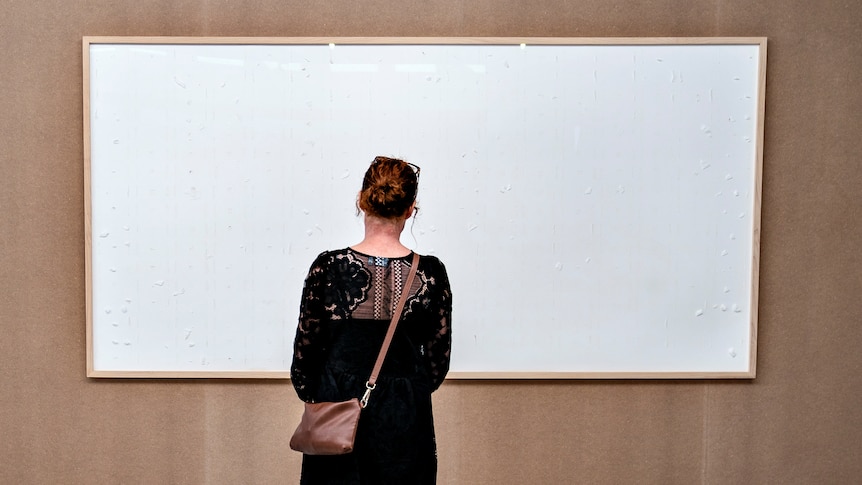 A woman stands in front of a blank canvas 