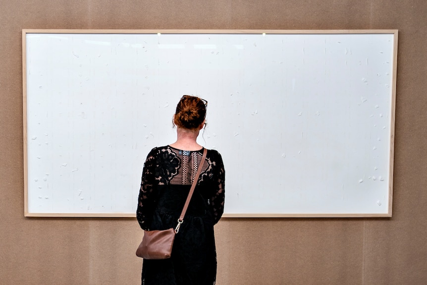A woman stands in front of a blank canvas 