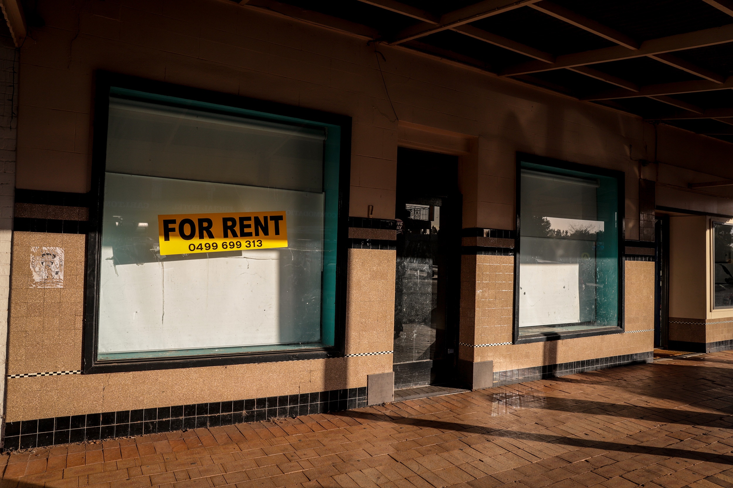 A vacant shop window with a yellow Rent sticker on a country street at sunrise