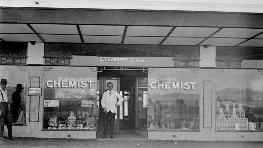 old black and white picture of a man standing in front of a chemist 