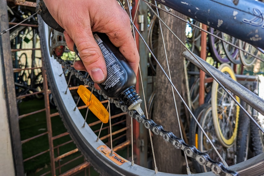 A close up shot of Andrew Stark's hands holding a bottle of lubricant above a bike chain
