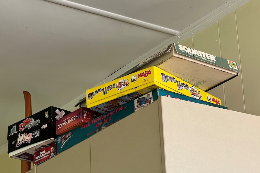 Board games sit stacked up high on top of a wardrobe.