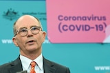 Paul Kelly speaks in front of a sign reading: Coronavirus (COVID-19)