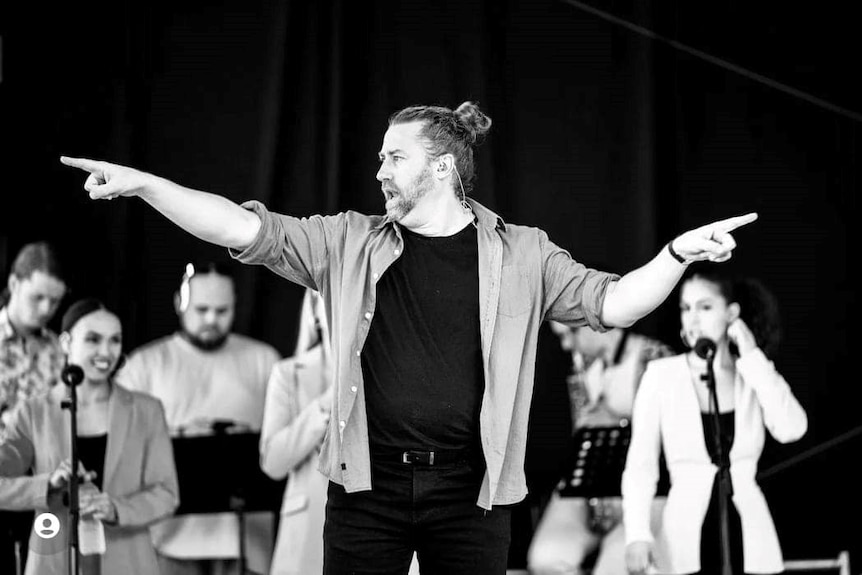 Black and white photo of an Auslan interpreter with a black T-shirt and a man bun working on stage