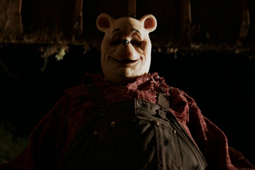 A person wearing a Winnie the Pooh mask looking down at the camera in a darkly-lit space.