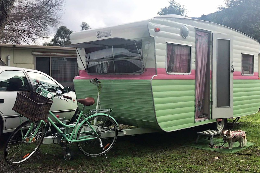 A caravan coloured white, pink and green parked next to a car.