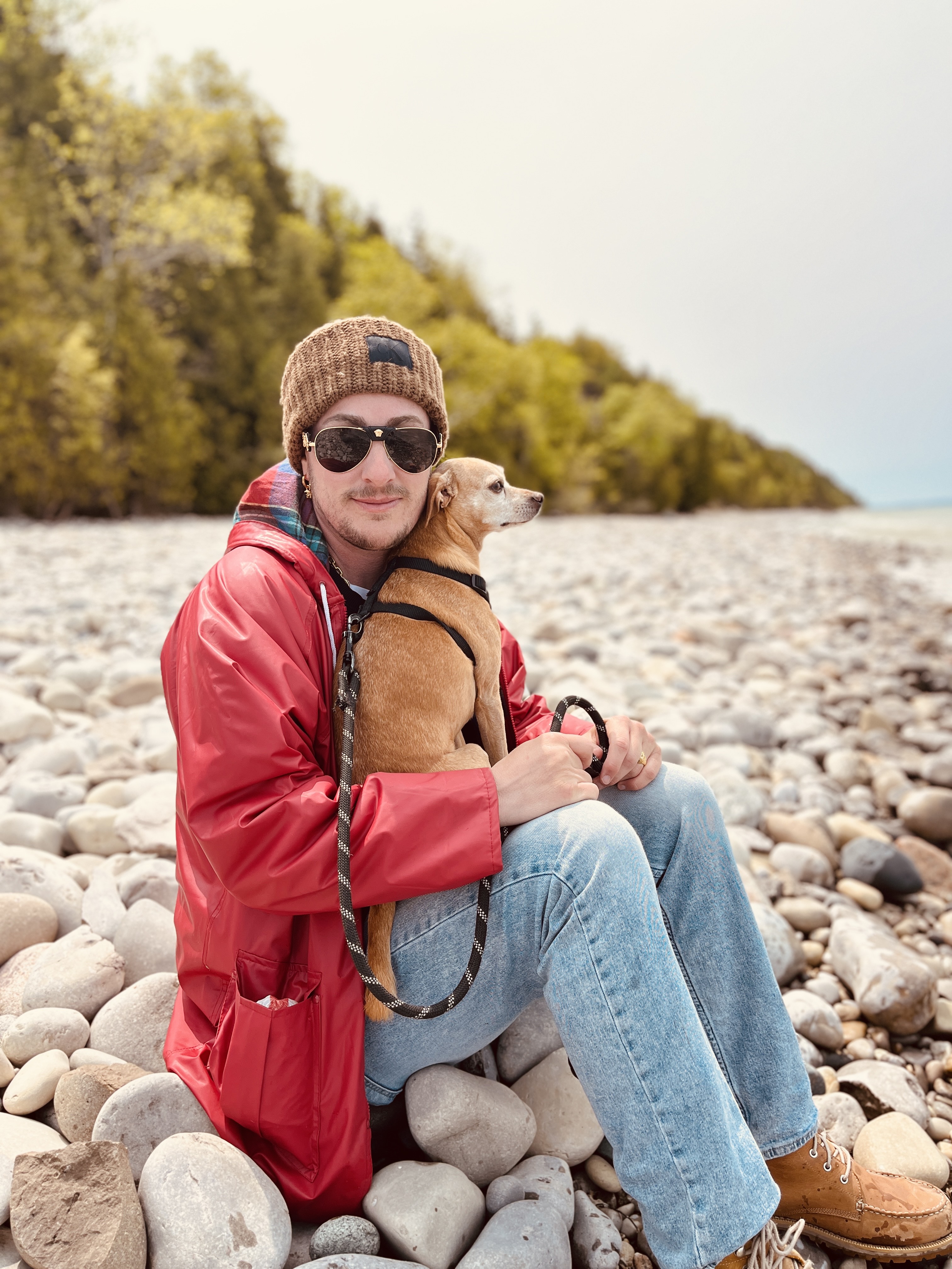 Leo smiles at the camera while sitting on some rocks and holds his dog in his lap