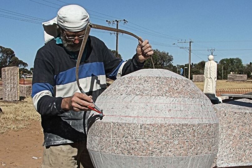 Man using compass to measure a sphere of granite rock that he is carving.