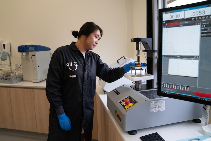 A woman places a burger patty within a scientific instrument.