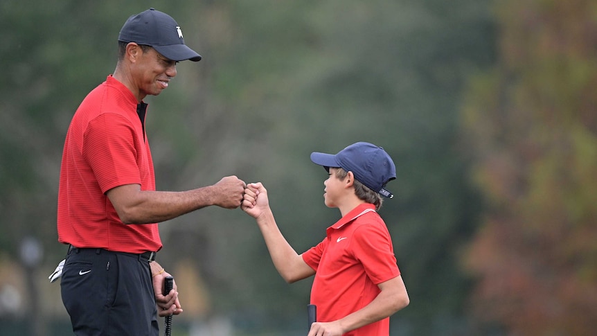Tiger Woods and Charlie Woods bump fists wearing red polo shirts