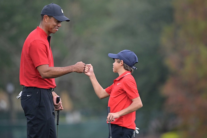 Tiger Woods and Charlie Woods bump fists wearing red polo shirts