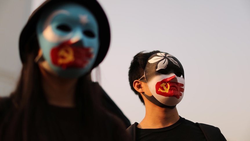 Two protesters wear masks emblazoned with the symbols of Hong Kong, the Communist Party and East Turkistan.