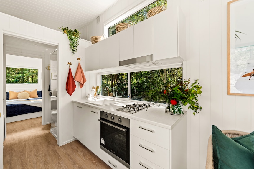 White tiny home kitchen interior with plants on bench and bedroom in background