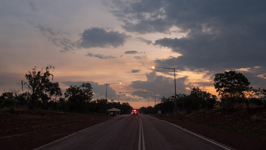 A cloudy sunset sky over a road with a police car with red lights stopped in it.