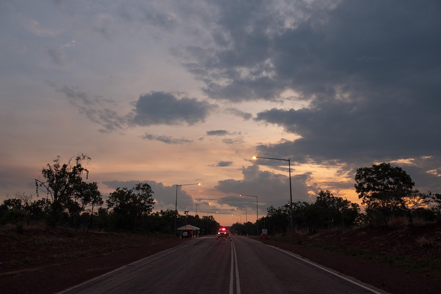 一条多云的日落天空在一条有​​红灯的警车停在它的道路上。