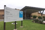 The front of the Eden Aged Care facility. A large sign, green grass and a small bed of roses.
