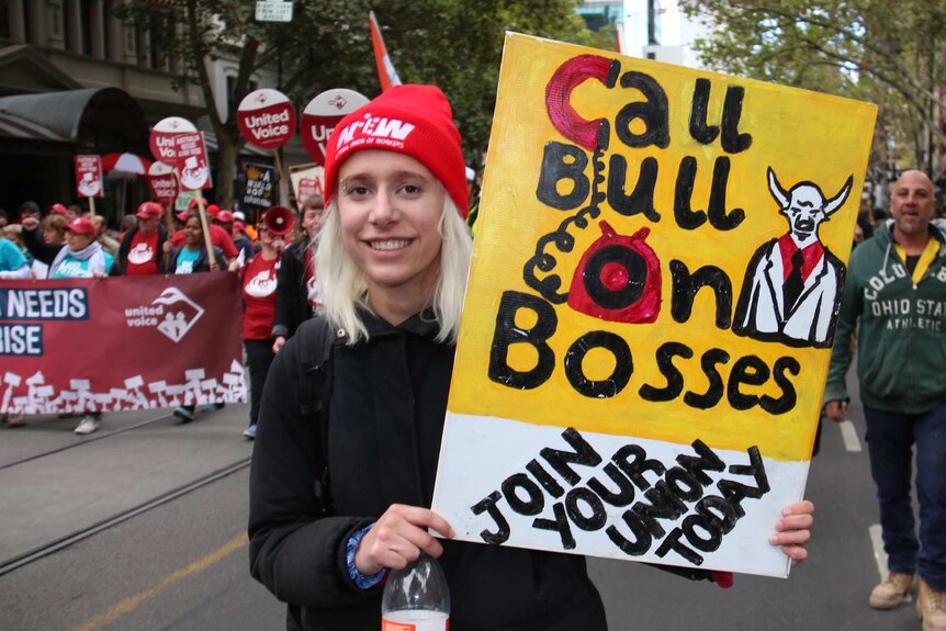 A young blonde woman woman holding a sign which reads 'call bull on bosses'.