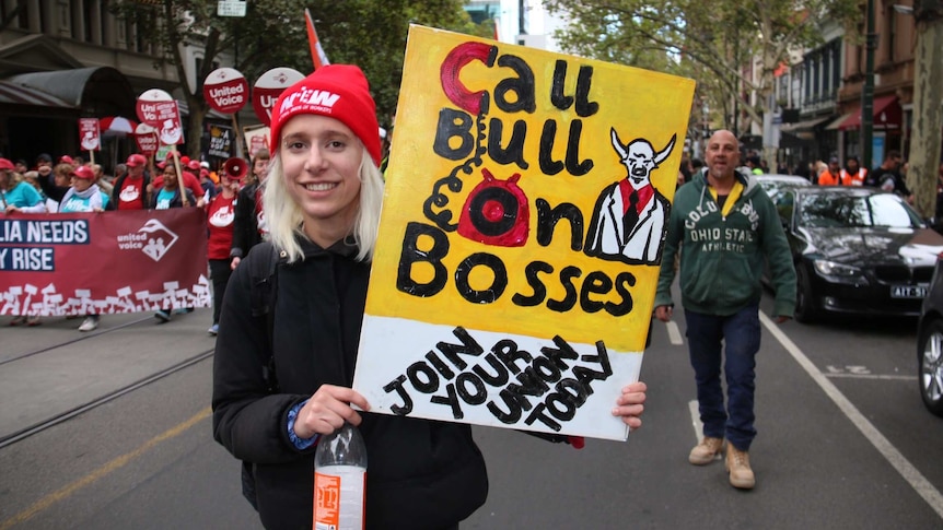 A young blonde woman woman holding a sign which reads 'call bull on bosses'.