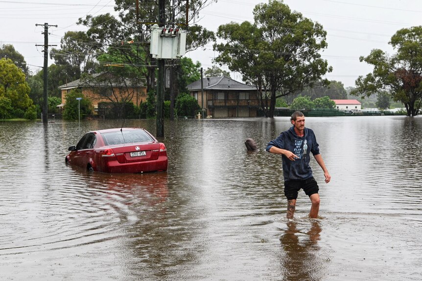 A man walks through flood water with a car in the background
