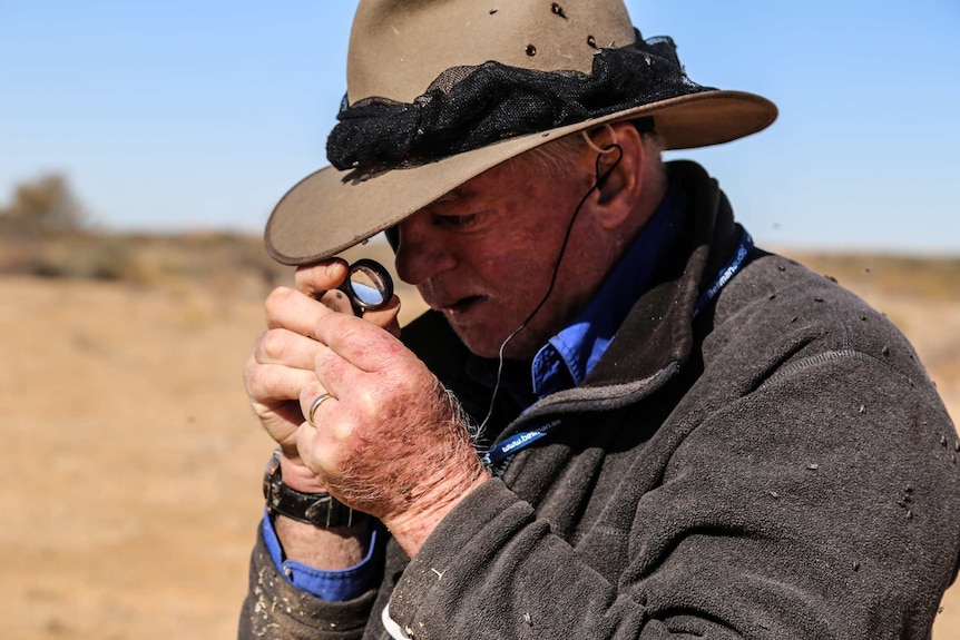 A man with an Akubra looks through a magnifying glass.